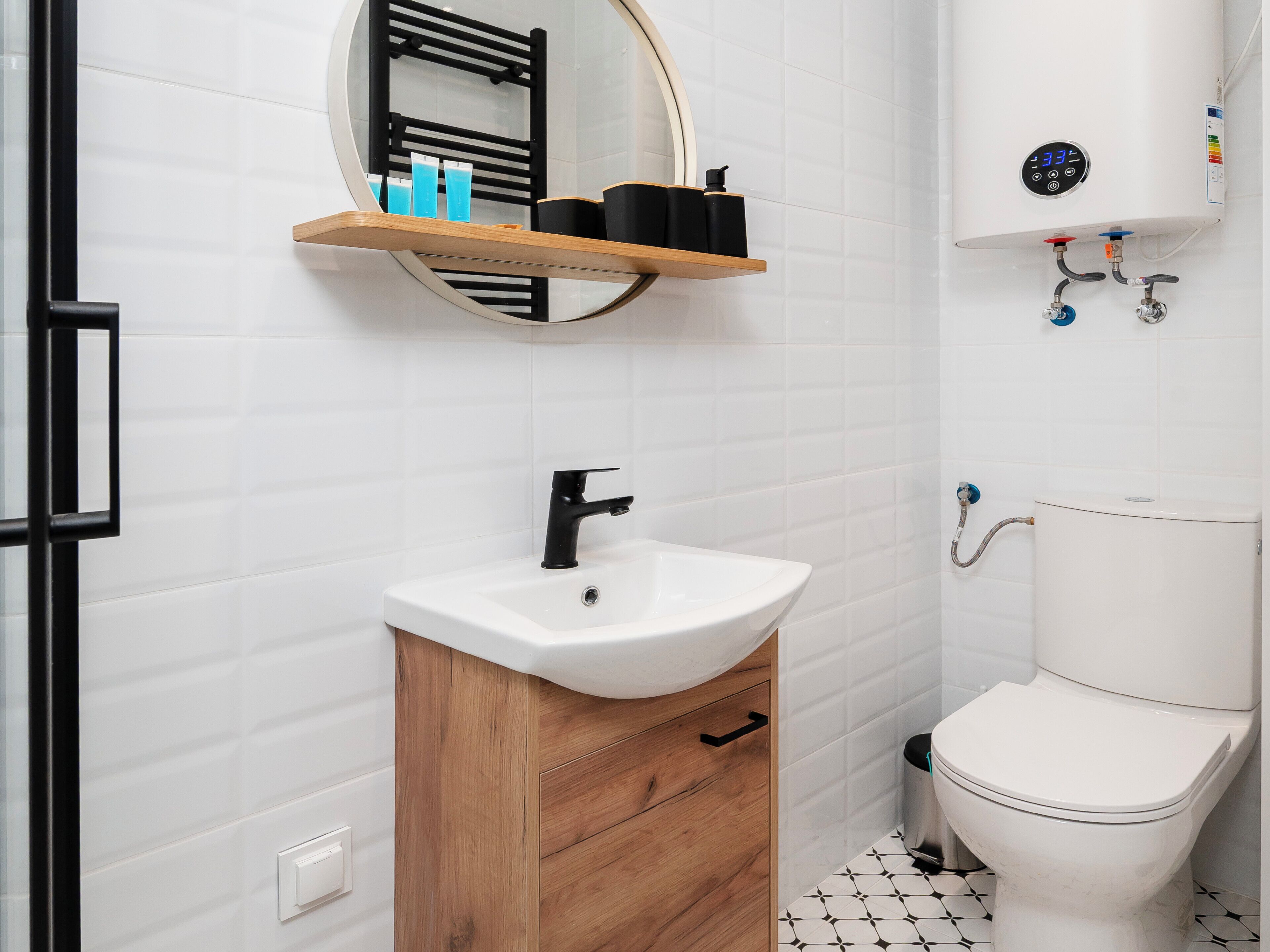 A bathroom with a white sink, black faucet, wooden cabinet, and a toilet. There is a shelf with toiletries above the mirror.