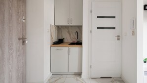 A hallway with a wooden door, a white door with horizontal stripes, and a kitchen area with cabinets and a countertop. - Marszałkowska City Centre Apartment (Warszawa)