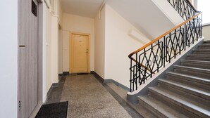 A hallway with a wooden door, a carpeted floor, and a staircase with a metal railing. - Marszałkowska City Centre Apartment (Warszawa)