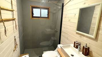 Ein kleines Badezimmer mit Holzvertäfelung, einer Toilette, einem Waschbecken mit Spiegel und einer Duschkabine.