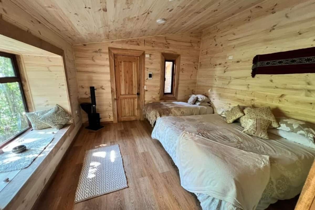 A wooden cabin bedroom with a bed, a window seat, and a door.