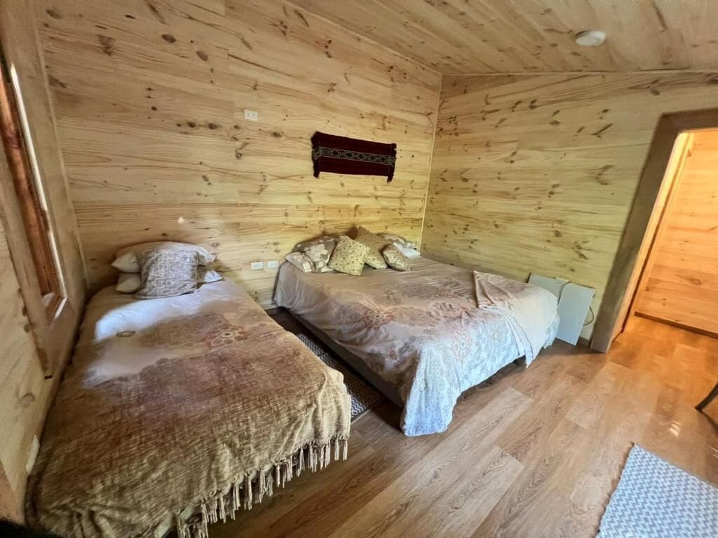 A wooden cabin room with two beds, a wooden ceiling, and a small rug on the floor.