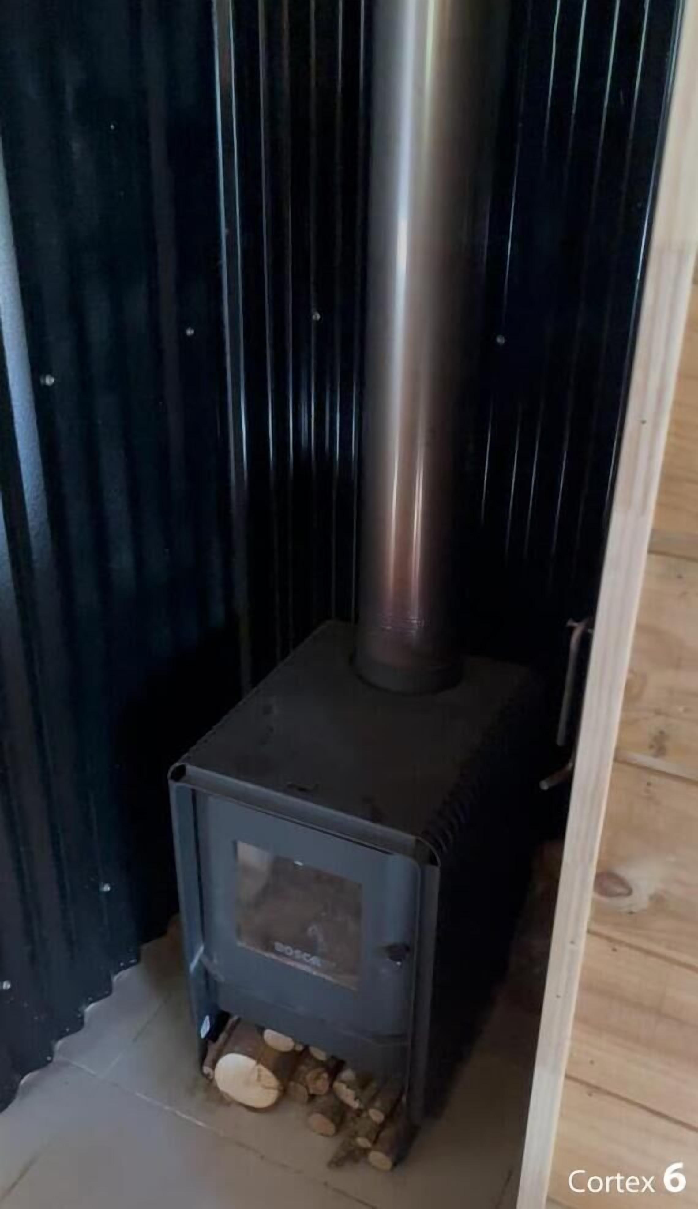 Un poêle à bois doté d’une cheminée en métal, placé contre un mur sombre près d’une fenêtre.