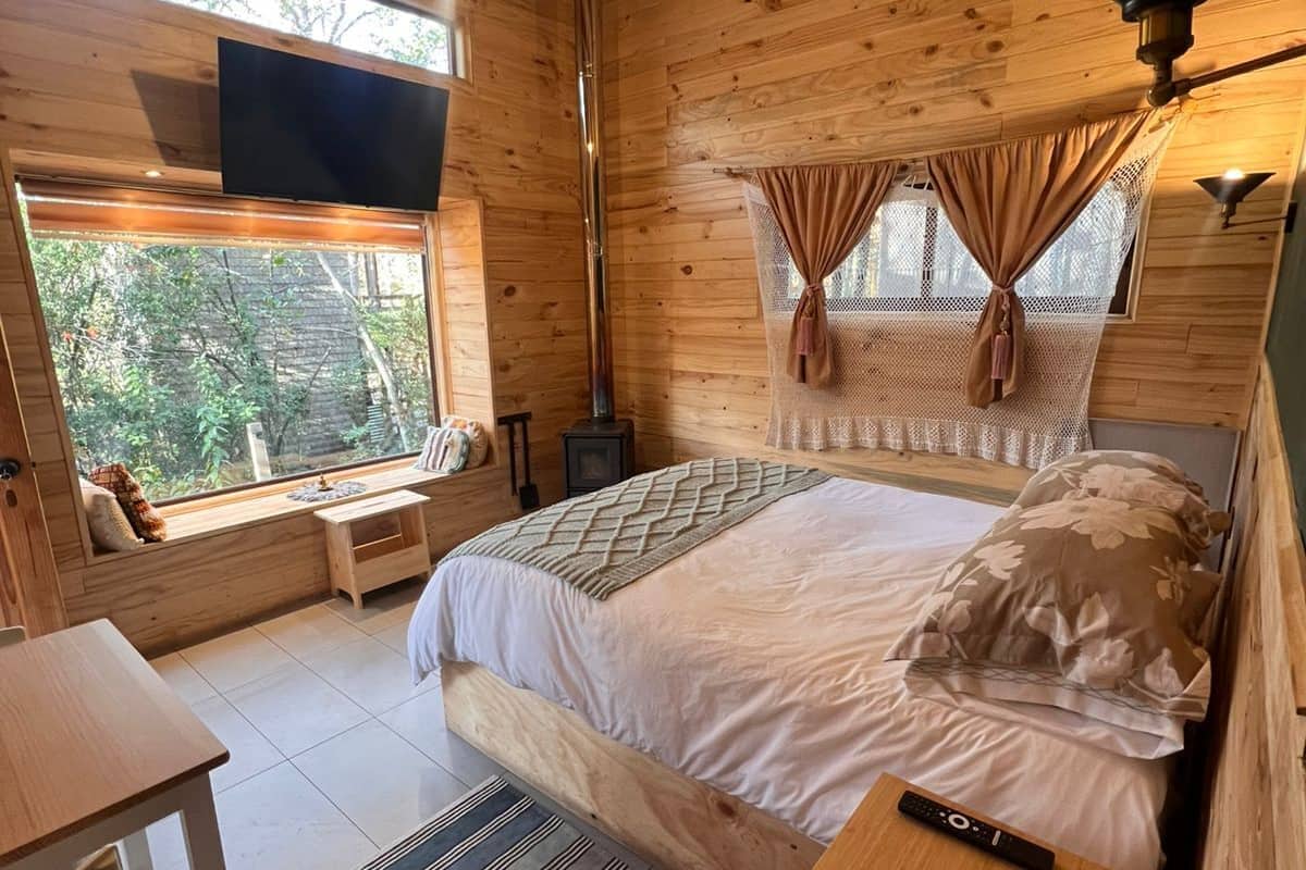 A cozy wooden cabin bedroom with a bed, a window seat, a TV, and a fireplace.