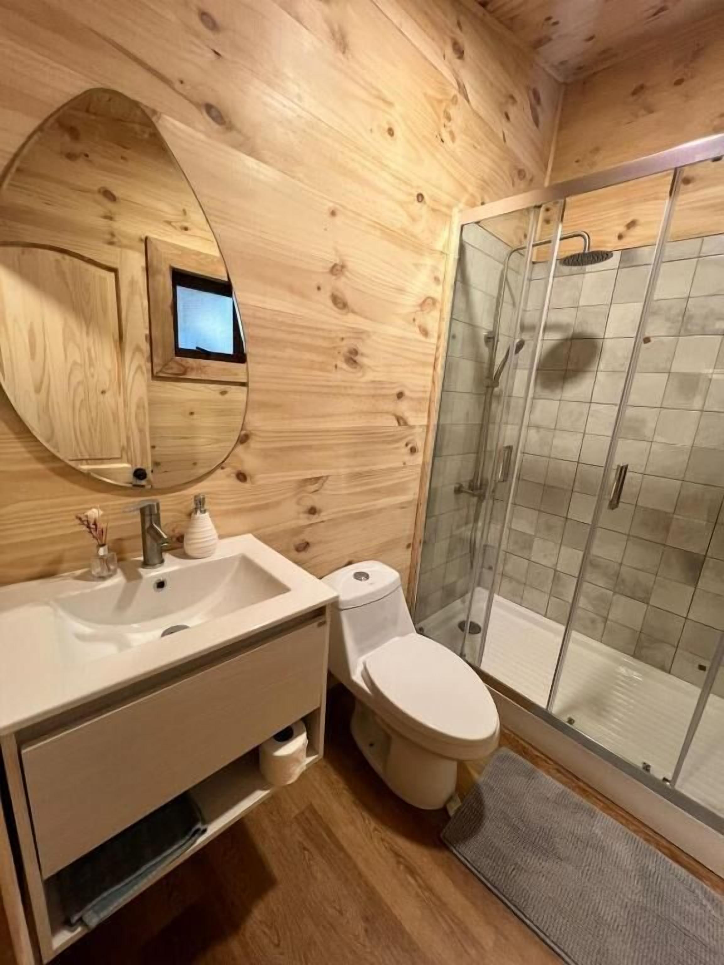 A wooden cabin bathroom with a sink, toilet, and glass-enclosed shower.