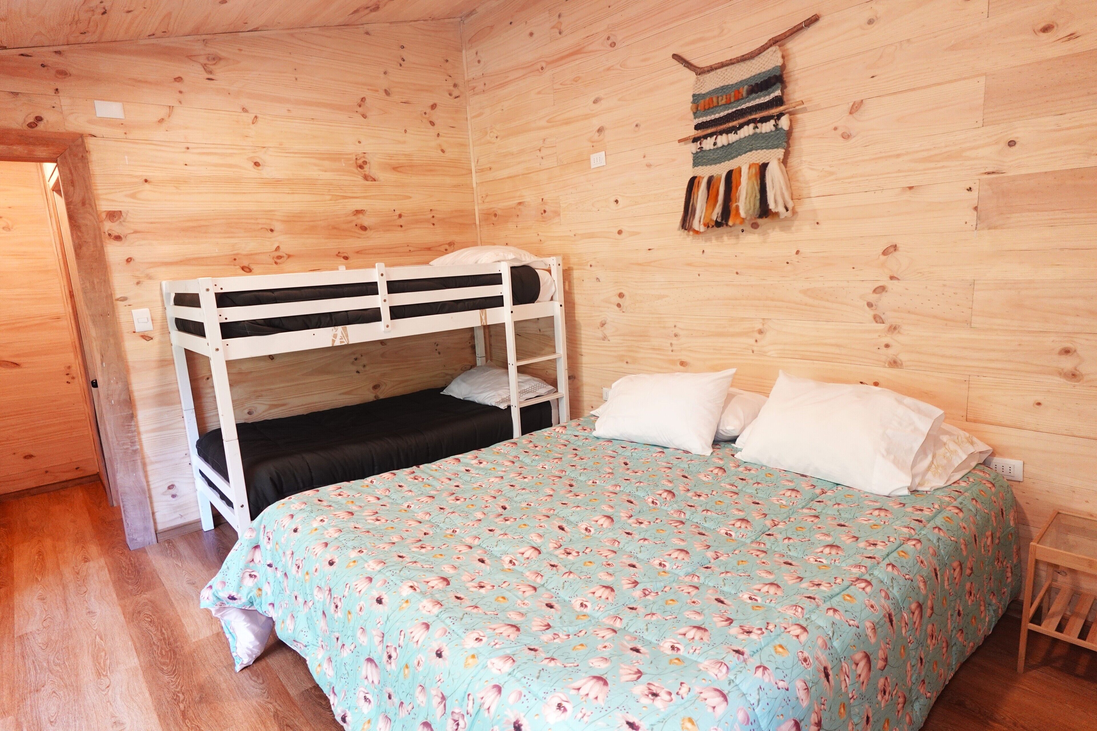 Una habitación de cabaña de madera con una litera, una cama individual con ropa de cama floral y un adorno colgado en la pared.