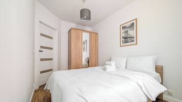Quarto com cama, guarda-roupa de madeira, espelho, quadro emoldurado e luminária no teto.