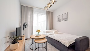 A modern bedroom with a bed, bedside table, and a small round table with a plant. - Artemskiej Comfort Apartment (Wrocław)