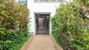 Une entrée moderne, avec une porte en verre, entourée d’une végétation luxuriante.