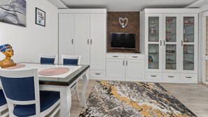Een moderne eethoek met een glazen tafel, witte kasten en een wandgemonteerde televisie.