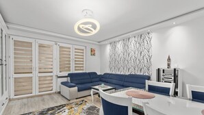 Een moderne woonkamer met een modulaire bank, een eettafel met stoelen, een kamerbreed tapijt en een decoratief wandobject.