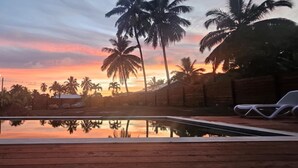 Une piscine dotée d’une terrasse en bois, entourée de palmiers et offrant une vue imprenable sur le coucher de soleil.