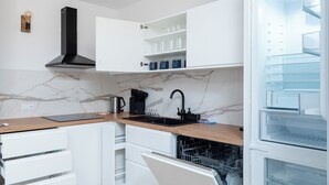 Moderni keittiö, jossa on valkoiset kaapit, puinen työtaso, sisäänrakennettu astianpesukone ja musta liesituuletin.