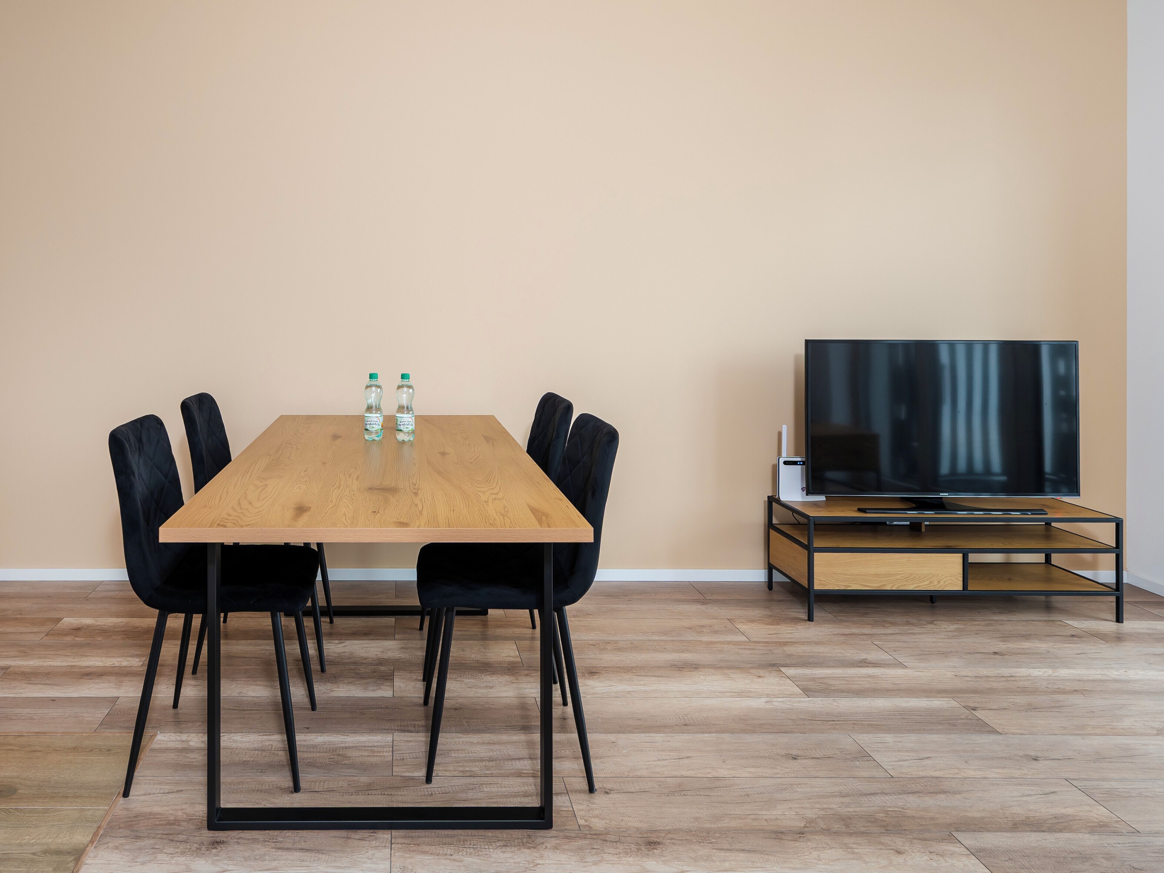 A modern dining area with a wooden table, black chairs, and a flat-screen TV on a stand.