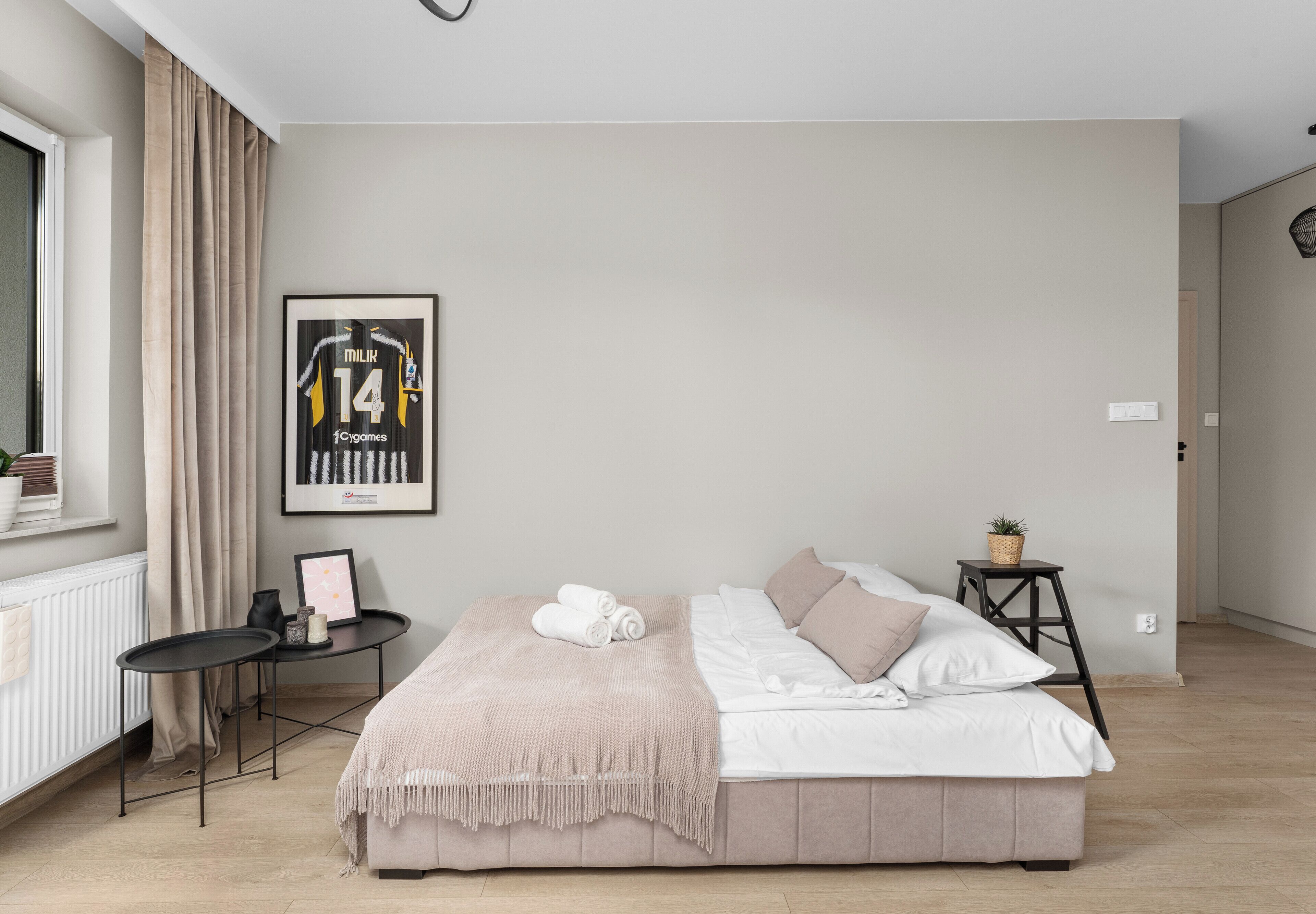 Un dormitorio ordenado con cama, mesitas de noche, un cuadro enmarco y un radiador.