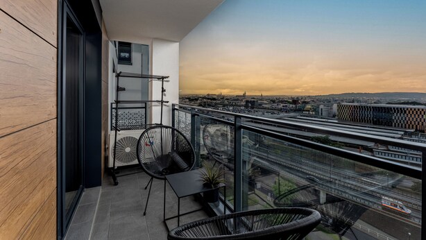A balcony with a city view, a small table, two chairs, a potted plant, and a fan. - Cracow Novum Apartment #496 (Kraków)