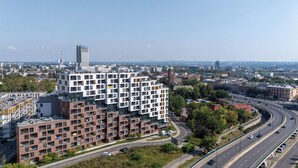 A modern apartment building with multiple floors and balconies, surrounded by a busy highway and other urban buildings. - Cracow Novum Apartment #365 (Kraków)