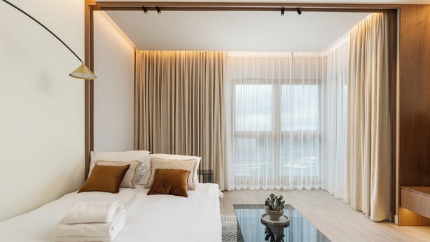 A modern hotel room with a large bed, a glass coffee table, and sheer curtains. - Cracow Novum Apartment #365 (Kraków)