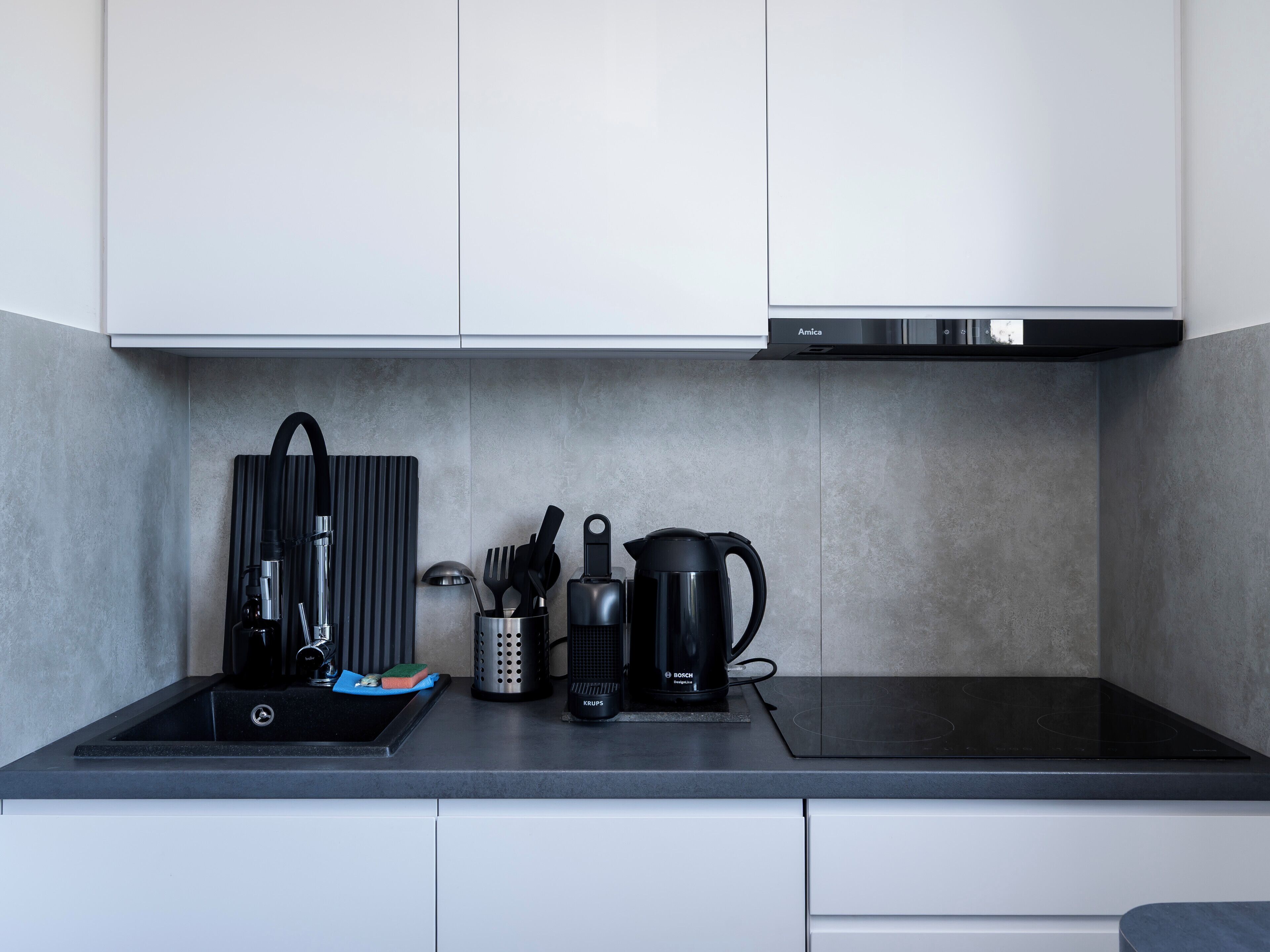 A modern kitchen with a black induction cooktop, a Bosch coffee maker, and a kettle.