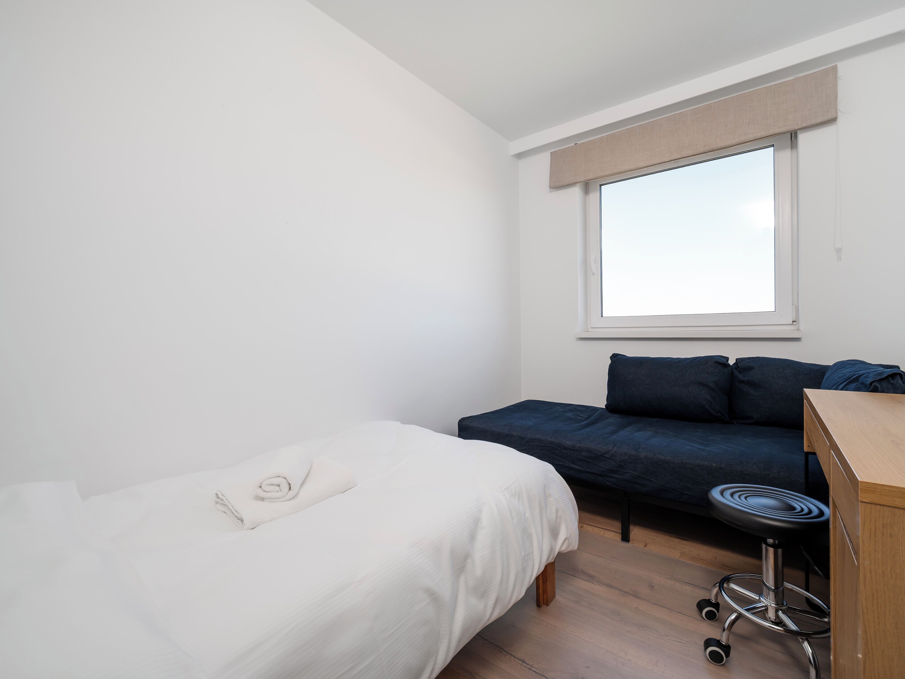 A small, clean room with a single bed, a sofa, and a desk with a chair.