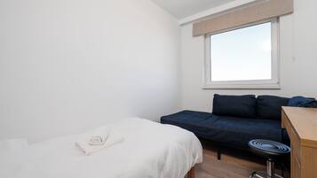 A small, clean room with a single bed, a sofa, and a desk with a chair.