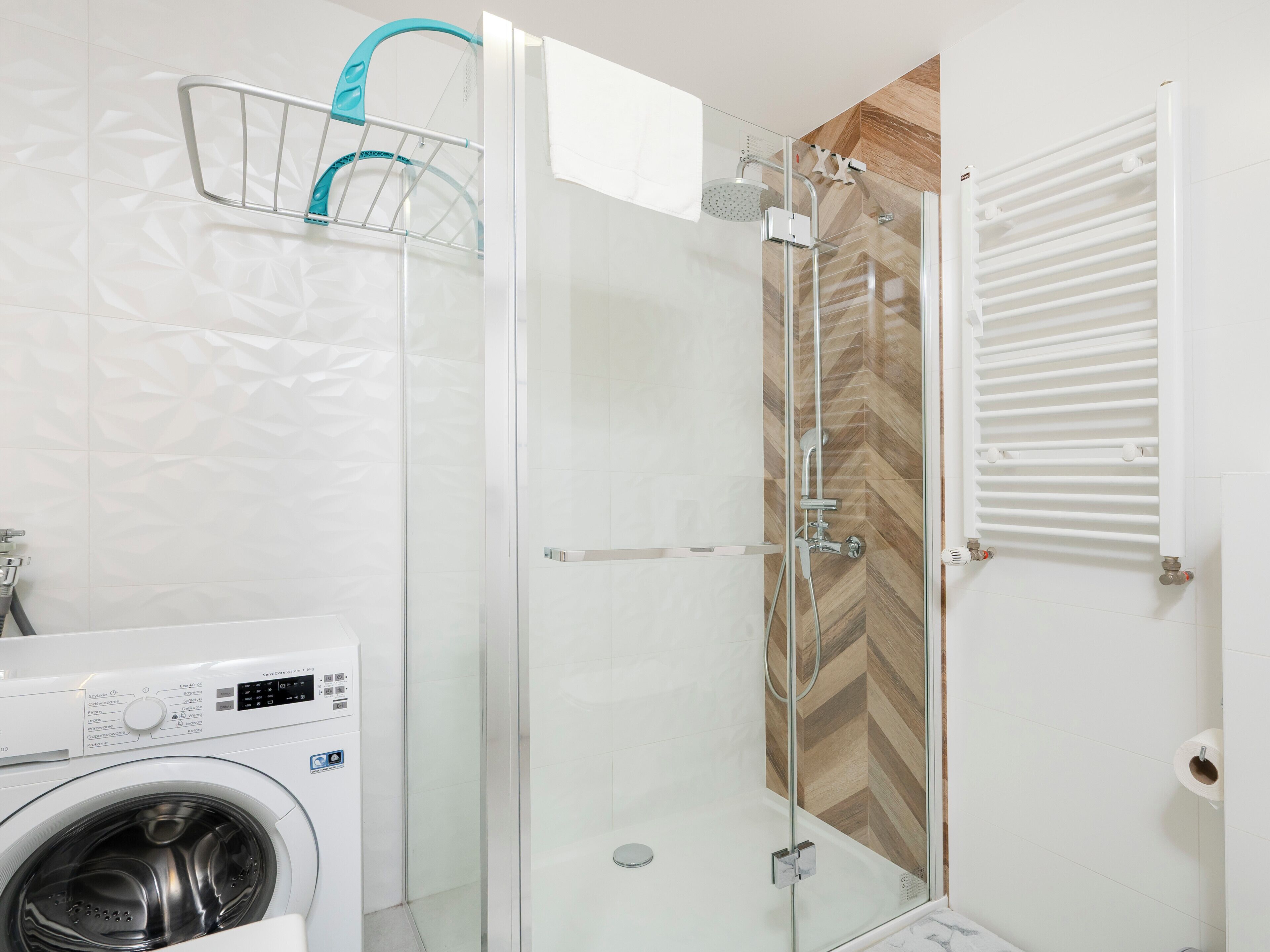 A modern bathroom with a glass-enclosed shower, a washing machine, and a towel rack.
