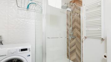 A modern bathroom with a glass-enclosed shower, a washing machine, and a towel rack.