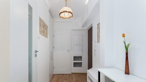 Um corredor com piso de madeira, paredes brancas, uma porta branca e um console branco com um vaso, além de um pendente.