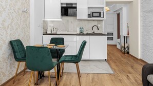 Uma cozinha moderna com armários brancos, uma ilha central e uma área de jantar com cadeiras estofadas em verde.