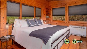 A wooden cabin bedroom with a bed, pillows, a bedside lamp, and a heater. - Basye Retreat - Authentic log cabin coziness! (Mount Jackson)