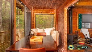 A cozy cabin interior with a wooden dining table, a cushioned bench, and a large window offering a forest view. - Basye Retreat - Authentic log cabin coziness! (Mount Jackson)