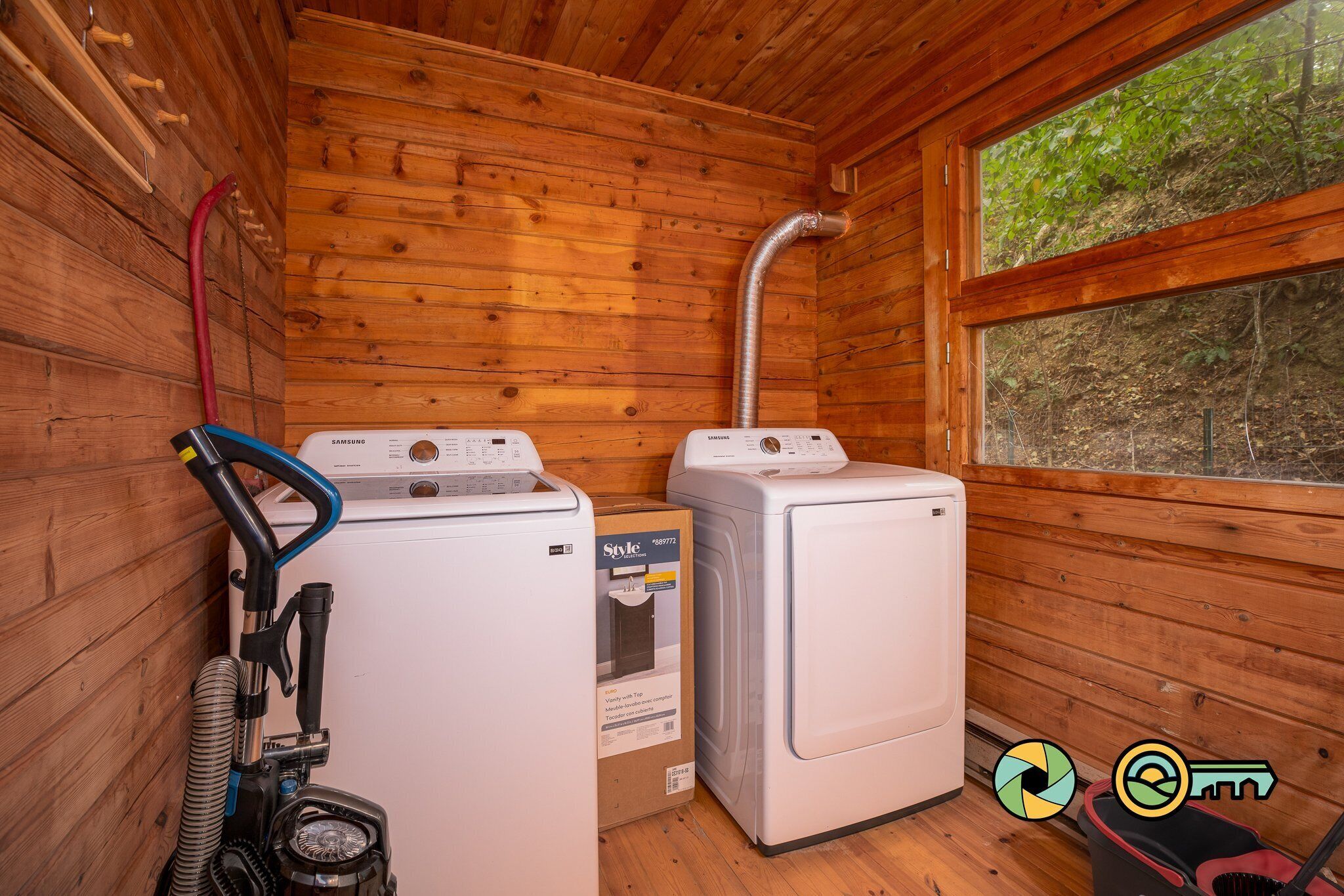 A small laundry room with two white washing machines, a vacuum cleaner, and a hose.