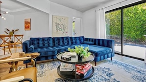 A modern living room with a blue sectional sofa, a coffee table with board games, and a dining area with wooden chairs and a table. - Casa Rafael: Palm Springs Private Pool & Hot Tub (Palm Springs)