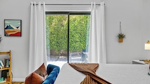 A bedroom with a large window, a bed, a blue sofa, and a bookshelf. - Casa Rafael: Palm Springs Private Pool & Hot Tub (Palm Springs)
