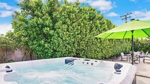 A hot tub with a green umbrella, surrounded by lush greenery and outdoor seating. - Casa Rafael: Palm Springs Private Pool & Hot Tub (Palm Springs)