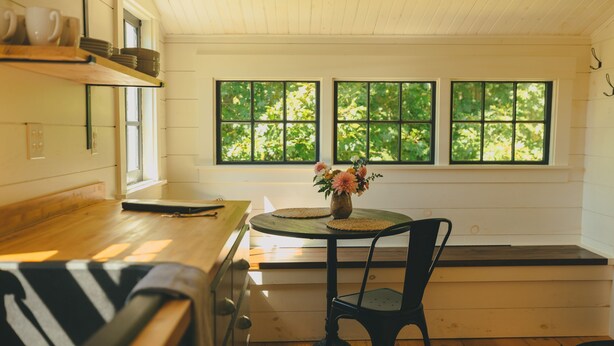 A kitchen with wooden countertops, a dining table with a chair, and a window with a view of greenery. - Peaceful Cottage on Maine Flower Farm (Buxton)