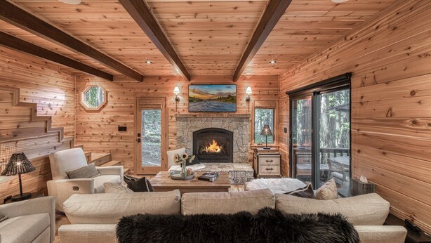 A cozy log cabin interior with a stone fireplace, wooden walls, and a comfortable seating area. - Songbird at Chambers by Tahoe Getaways - Pet-Friendly 2 BR w/ HOA Beach Pool (Homewood)