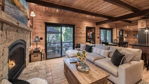 A cozy cabin interior with a stone fireplace, wooden ceiling beams, a sofa, and a dining area. - Songbird at Chambers by Tahoe Getaways - Pet-Friendly 2 BR w/ HOA Beach Pool (Homewood)