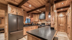 A modern kitchen with wooden cabinetry, a stainless steel refrigerator, and a granite countertop. - Songbird at Chambers by Tahoe Getaways - Pet-Friendly 2 BR w/ HOA Beach Pool (Homewood)