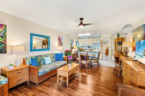 A spacious living area with a sofa, coffee table, and wooden side tables. A dining area with chairs and a table is visible in the background.