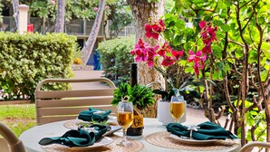 A round table set outdoors with a bottle, two glasses, and a potted plant. - Tropical Charm by Napili Beach (Napili)