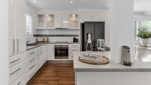 A modern kitchen with white cabinetry, a built-in oven, and a central island with a welcome sign. - Wave Whisperer - 1/15 Kingscliff (Tweed)