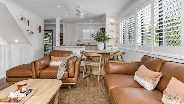A modern living room with a brown leather sofa, a wooden coffee table, and a dining area with a wooden table and chairs. - Wave Whisperer - 1/15 Kingscliff (Tweed)