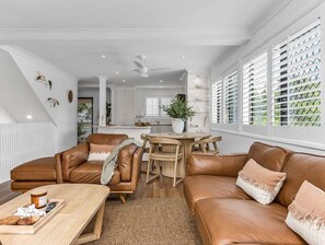 A modern living room with a brown leather sofa, a wooden coffee table, and a dining area with a wooden table and chairs. - Wave Whisperer - 1/15 Kingscliff (Tweed)