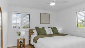 A bedroom with a bed, a nightstand, a lamp, and a window with blinds. - Wave Whisperer - 1/15 Kingscliff (Tweed)
