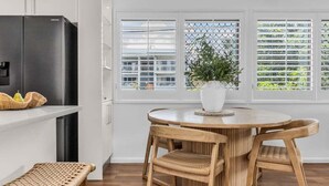 A modern kitchen with a black refrigerator, a round wooden table with chairs, and a potted plant. - Wave Whisperer - 1/15 Kingscliff (Tweed)