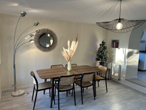A dining area with a wooden table, six chairs, a tall floor lamp, a wall-mounted mirror, and a small Christmas tree.