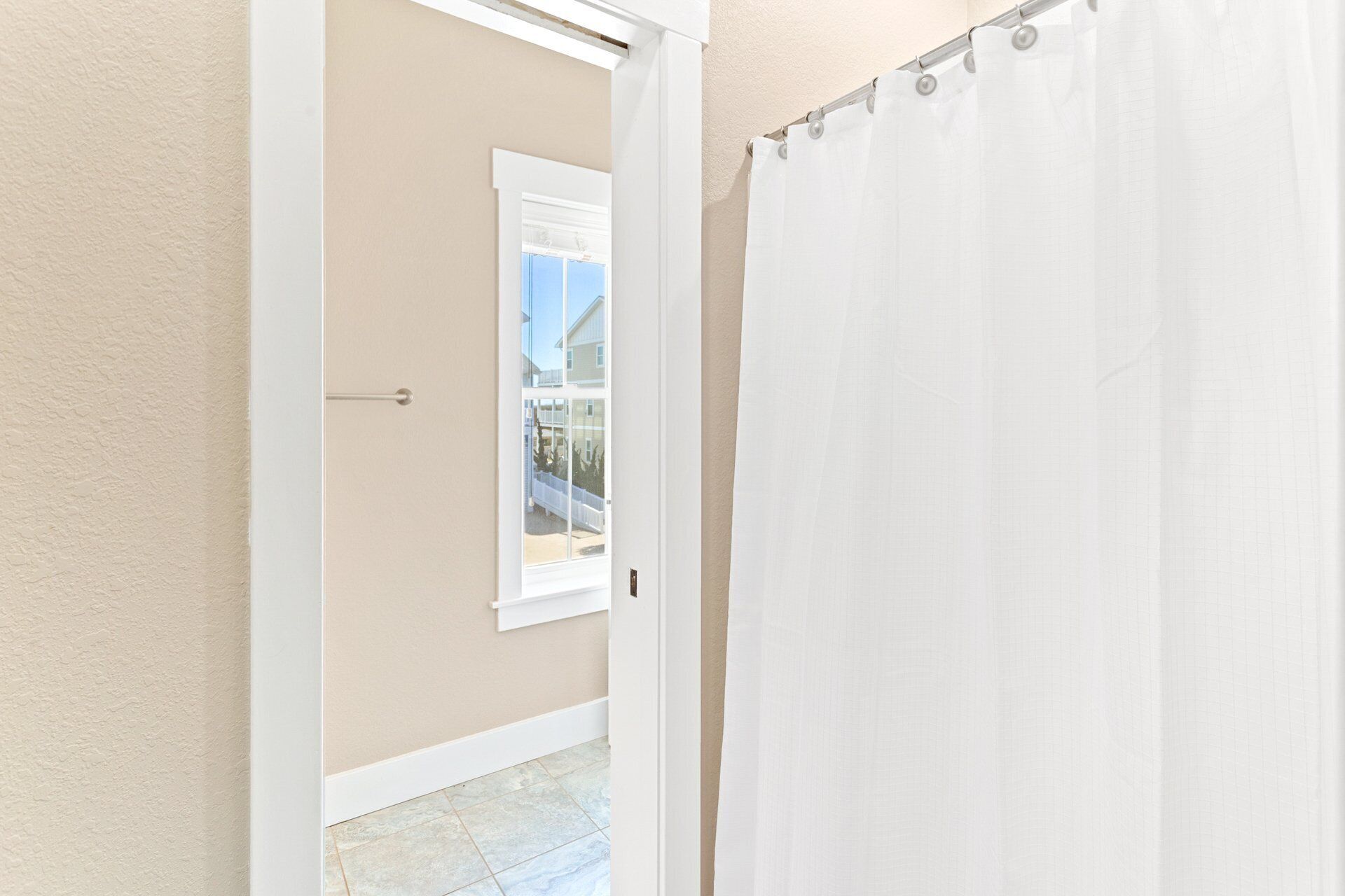 A hallway with a white door, a window with a view of a balcony, and a white shower curtain.