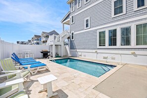 A swimming pool with lounge chairs, a barbecue grill, and a white fence.