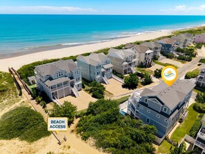 A coastal residential area with beachfront access, featuring multi-story houses with balconies, a sandy beach, and a clear view of the ocean.